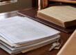 Documentos imobiliários, chave e livro registral sobre mesa de madeira.